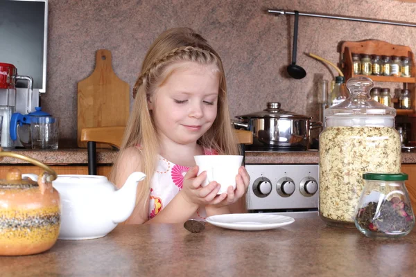 Little girl drinks tea from cup at kitchen — Stock Photo, Image