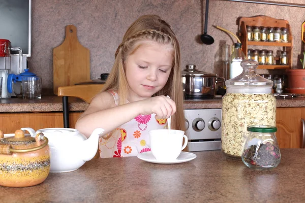 Malá holka pije čaj z poháru v kuchyni — Stock fotografie
