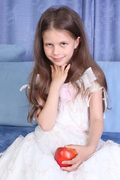 Little girl sitting in sofa with apple — Stock Photo, Image