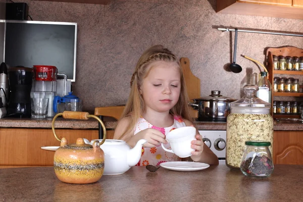 Little girl drinks tea from cup at kitchen — Stock Photo, Image