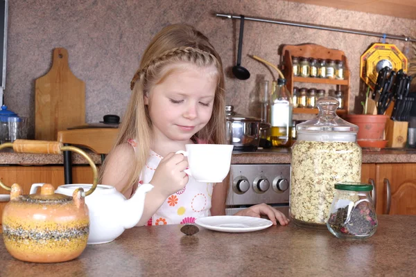 Little girl drinks tea from cup at kitchen — Stock Photo, Image