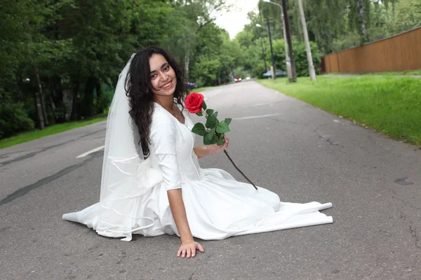 Bride with a rose sitting on a road — Stock Photo, Image