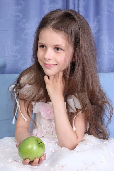 Liten flicka sitter i soffan med äpple — Stockfoto