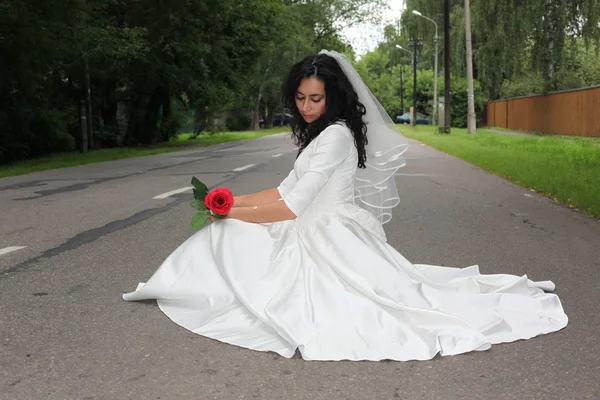 Bride with rose hitchhiking on a road — Stock Photo, Image
