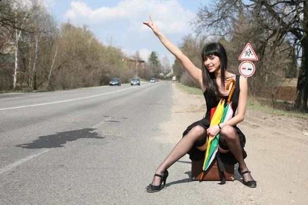 Chica en el camino sentarse en la parte superior de la maleta vintage con paraguas — Foto de Stock