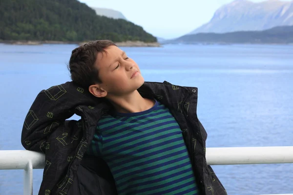 Niño reflexivo se para a bordo de la nave y mira el hermoso paisaje — Foto de Stock