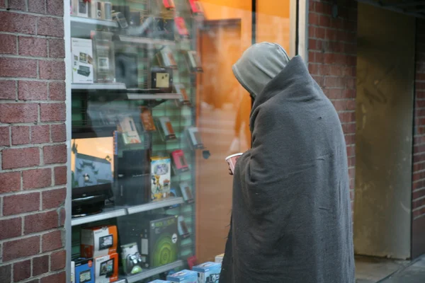 Homeless man stands in front of shop window — Stock Photo, Image