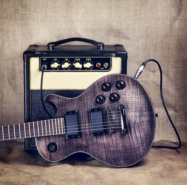 Black electric guitar and amplifier on brown canvas background