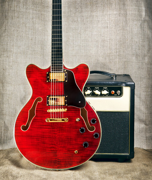 Red semi-hollow electric guitar and amplifier on brown canvas background