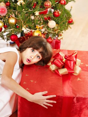 Çocuk Noel ağacının yanında hediye kutusu.