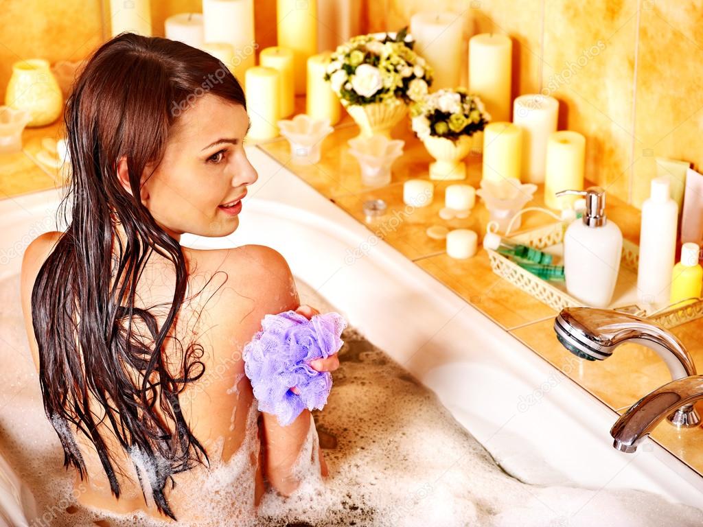 Woman using bath sponge in bathtub.
