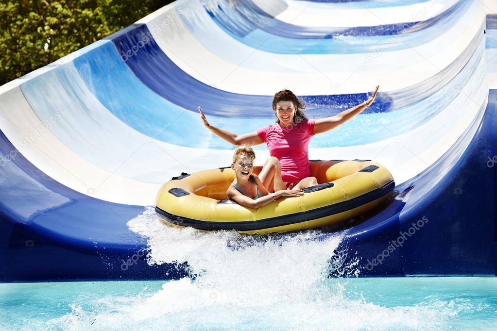 Child with mother on water slide at aquapark.