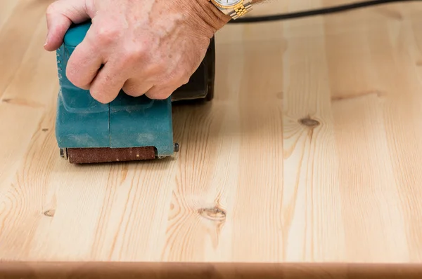 Mans hand on belt sander on pine wood — Stock Photo, Image