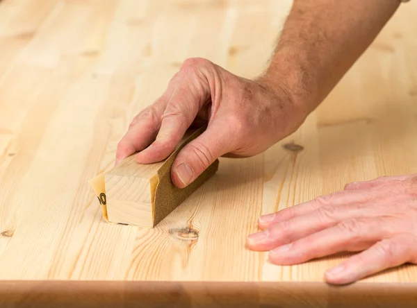 Mans hand on sanding block on pine wood — Stock Photo, Image