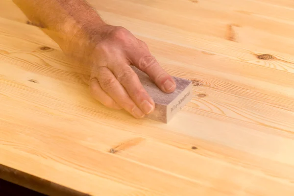 Mans hand on sanding block on pine wood — Stock Photo, Image