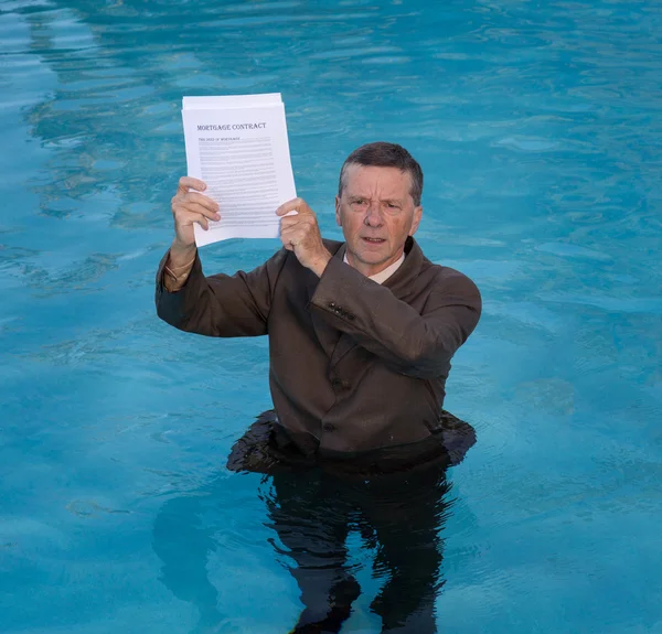Senior hombre sosteniendo el documento del préstamo hipotecario en el agua —  Fotos de Stock