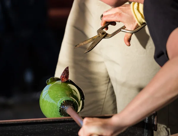 Glass blower works on ornate green bottle