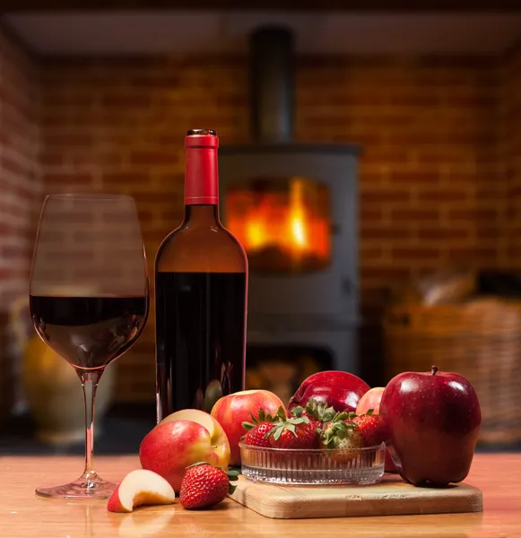 Красное вино и фрукты перед горящим огнем — стоковое фото