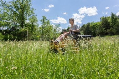 Senior man on zero turn lawnmower in meadow