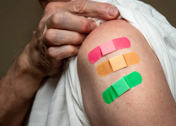 Senior man holding up shirt showing three covid-19 vaccine injections — Stockfoto