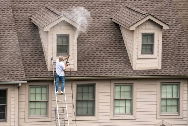 Painter on ladder using pressure wash spray to clean woodwork before painting townhome