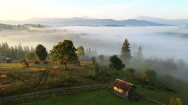 İnsansız hava aracı sabah sisiyle kaplı bir dağ köyünün üzerinden uçuyor. Karpat Dağları, Ukrayna, Avrupa. Sinematik hava çekimi. Toprağın güzelliğini keşfedin. 4k, İHA videosu ile çekilmiştir..