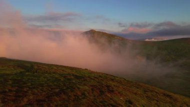 İnsansız hava aracı sabah güneşiyle dağları kaplayan sisin üzerinde uçuyor. 4k, İHA videosu.