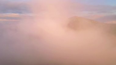 İnsansız hava aracı sabah güneşiyle dağları kaplayan sisin üzerinde uçuyor. 4k, İHA videosu.