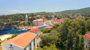 İnsansız hava aracı güneşli bir günde eski Veli Losinj kasabasında mavi bir körfezin üzerinde uçuyor. Hırvatistan. 4k, İHA videosu ile çekilmiştir..