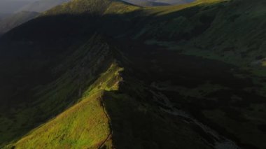 Güneş tarafından kuşbakışı aydınlatılan bir dağ silsilesinin yaz manzarası. Karpat Dağları, Ukrayna, Avrupa. Sinematik hava çekimi. Dünyanın güzelliği. 4k, İHA videosu ile çekilmiştir..