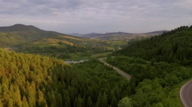 İnsansız hava aracı dağların arasından geçen dolambaçlı bir yolda uçuyor. Karpat Dağları, Ukrayna, Avrupa. Sinematik hava çekimi. Toprağın güzelliğini keşfedin. 4k, İHA videosu ile çekilmiştir..