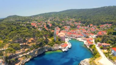İnsansız hava aracı güneşli bir günde eski Veli Losinj kasabasında mavi bir körfezin üzerinde uçuyor. Hırvatistan. 4k, İHA videosu ile çekilmiştir..