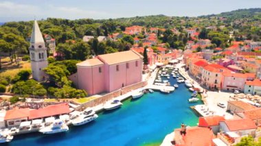 İnsansız hava aracı güneşli bir günde eski Veli Losinj kasabasında mavi bir körfezin üzerinde uçuyor. Hırvatistan. 4k, İHA videosu ile çekilmiştir..