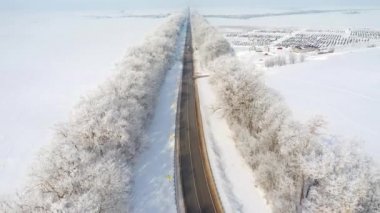 Hava aracı güneşli bir günde karlı arazilerden geçen otobanın üzerinde uçar. 4k 'lık bir videoda çekildi.