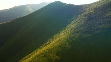İnsansız hava aracı güneşin aydınlattığı yeşil dağ sıralarının üzerinden uçar. 4k 'lık bir videoda çekildi.