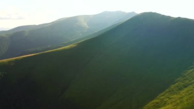 İnsansız hava aracı güneşin aydınlattığı yeşil dağ sıralarının üzerinden uçar. 4k 'lık bir videoda çekildi.