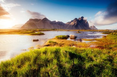 Güneş ışığıyla parlayan yeşil tepelerin güzel manzarası. Dramatik ve muhteşem bir sahne. Bulunduğu yer Stoksnes Burnu, Vestrahorn (Batman Dağı), İzlanda, Avrupa. Sıcak tonlama. Güzellik dünyası.