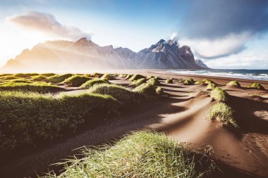 Güneş ışığıyla parlayan alışılmadık tepeler. Dramatik ve muhteşem bir sahne. Turist eğlencesi. Stoksnes Burnu, Vestrahorn (Mt. Batman), İzlanda, Avrupa. Bağbozumu etkisi. Instagram filtresi. Güzellik dünyası.