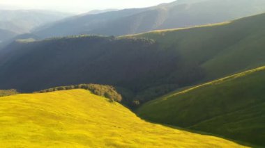 İnsansız hava aracı güneşin aydınlattığı yeşil dağ sıralarının üzerinden uçar. 4k 'lık bir videoda çekildi.