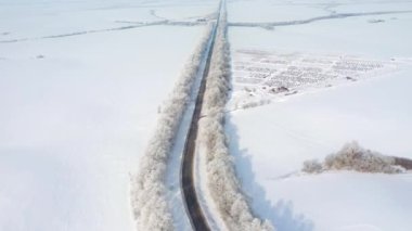 Hava aracı güneşli bir günde karlı arazilerden geçen otobanın üzerinde uçar. 4k 'lık bir videoda çekildi.