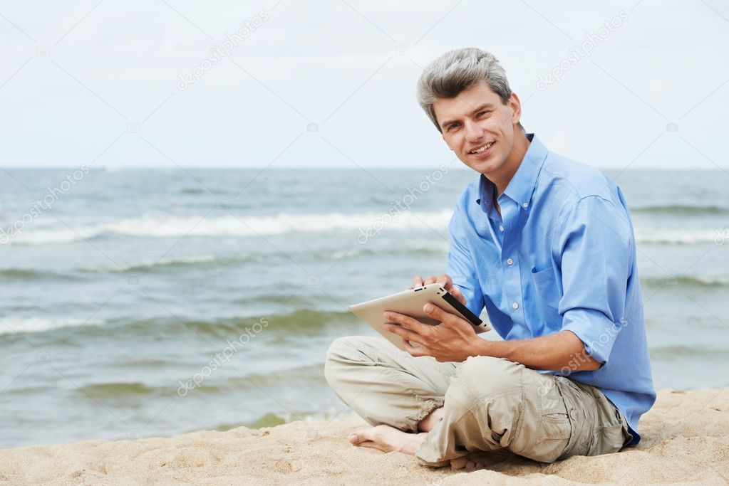 Young smiling man with tablet pc on seashore