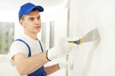 Plasterer with putty knife at wall filling clipart