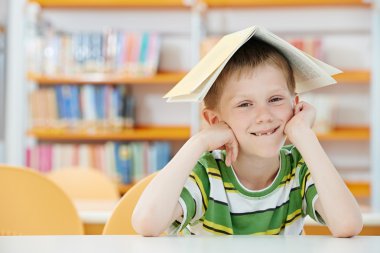Young boy with book in library clipart