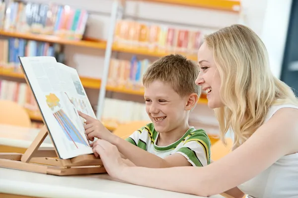 Młoda kobieta i chłopiec czytanie książki w bibliotece — Zdjęcie stockowe