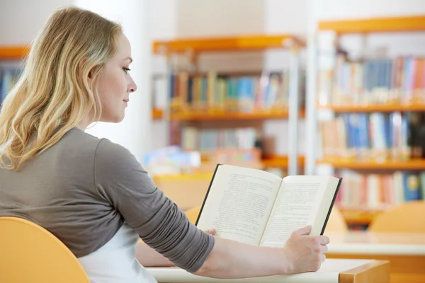 Jonge vrouw die boek leest in bibliotheek — Stockfoto