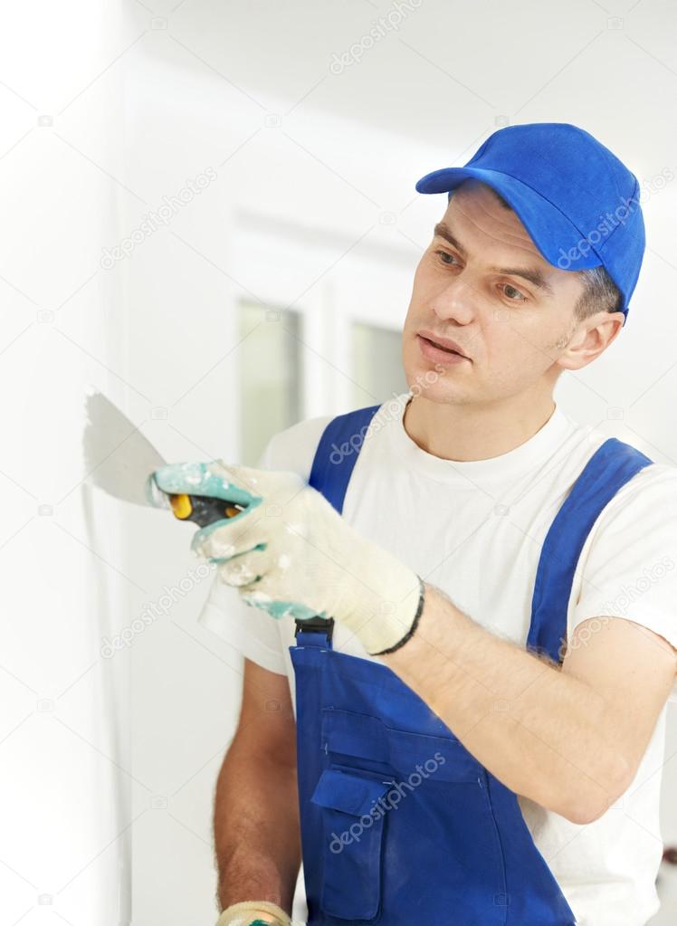 Plasterer with putty knife at wall filling