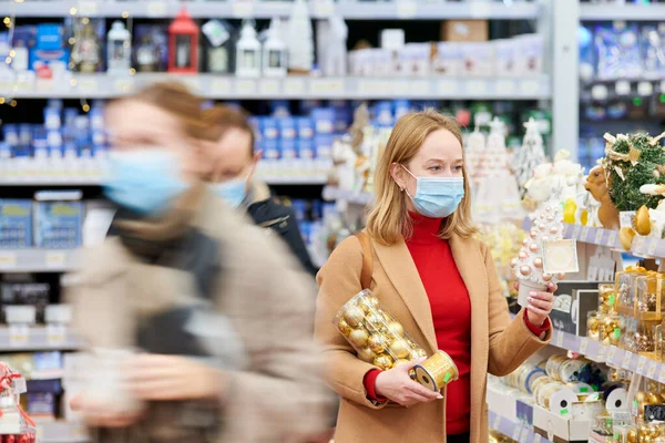 Weihnachtsdekoration einkaufen. Frau in Maske kauft Neujahrsdekor im Geschäft — Stockfoto