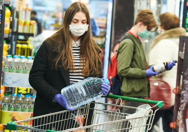 Hombre con máscara y guantes de protección comprar tienda de agua en coronavirus epidemia —  Fotos de Stock