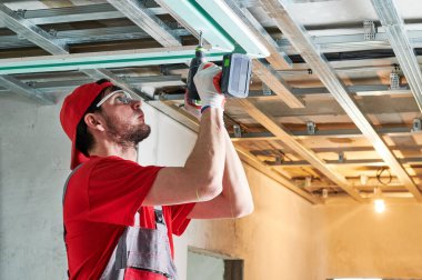 Alçıtaşı alçıtaşı kurulumu. Alçıpan evde çalışıyor. Müteahhit işçiler apartman geliştirme sırasında tavanda metal çerçeve tornavida