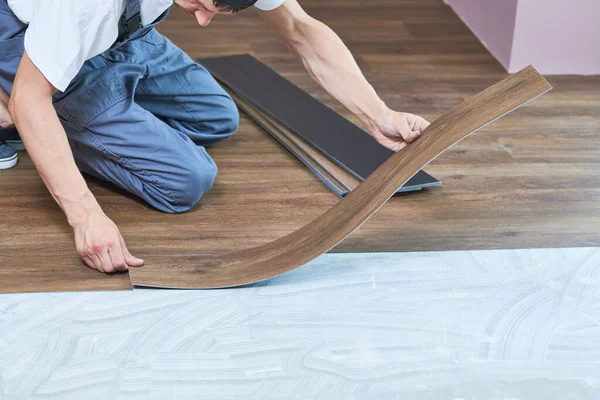 indoor floor installation. carpenter worker installing vinyl floor tiles with wood decoration,